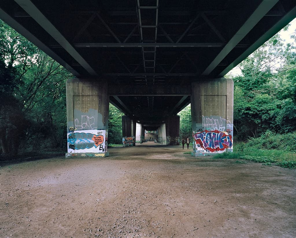 Graffiti and tags cover the concrete pillars of the motorway above