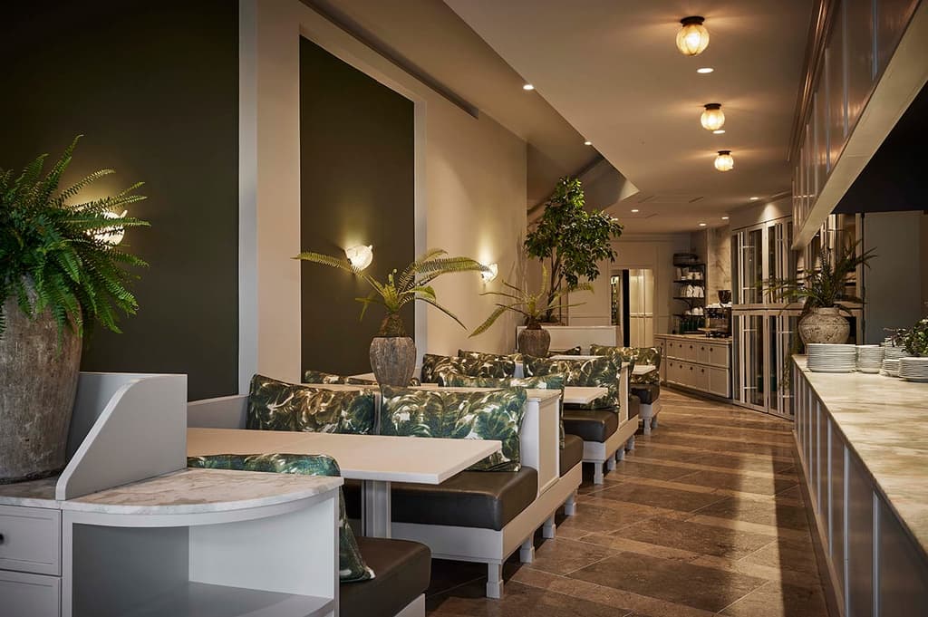 In the galley dining area, seating features botanically-themed upholstery and cushions, ferns and large-leaf evergreen plants